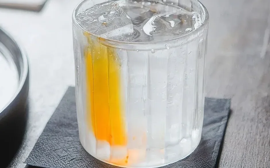 Verre d’eau glacée dans lequel une coloration orange se dissout lentement.
