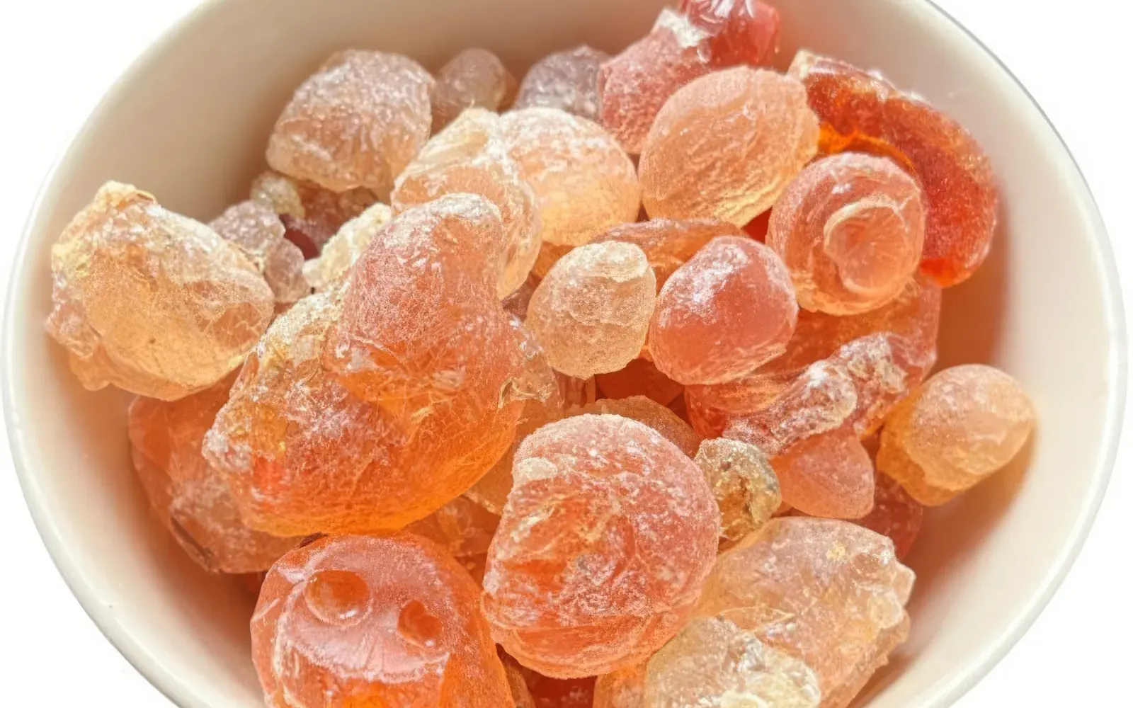 Bol blanc rempli de nodules ambrés de gomme arabique brute.