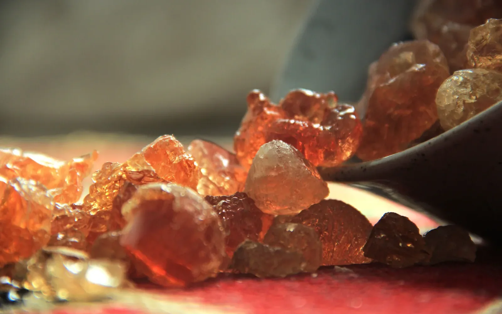 Gros plan de nodules ambrés de gomme arabique au bord d’un récipient sombre.